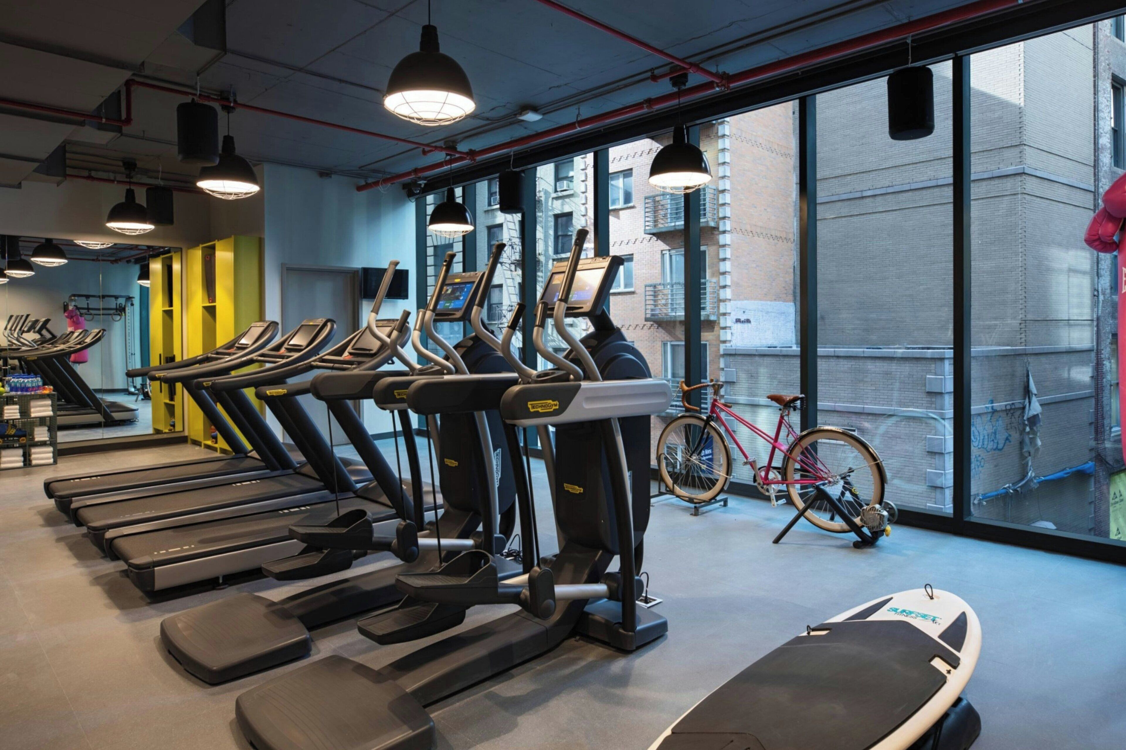 Un gimnasio con cintas de correr, bicicletas estáticas y una máquina de remo.