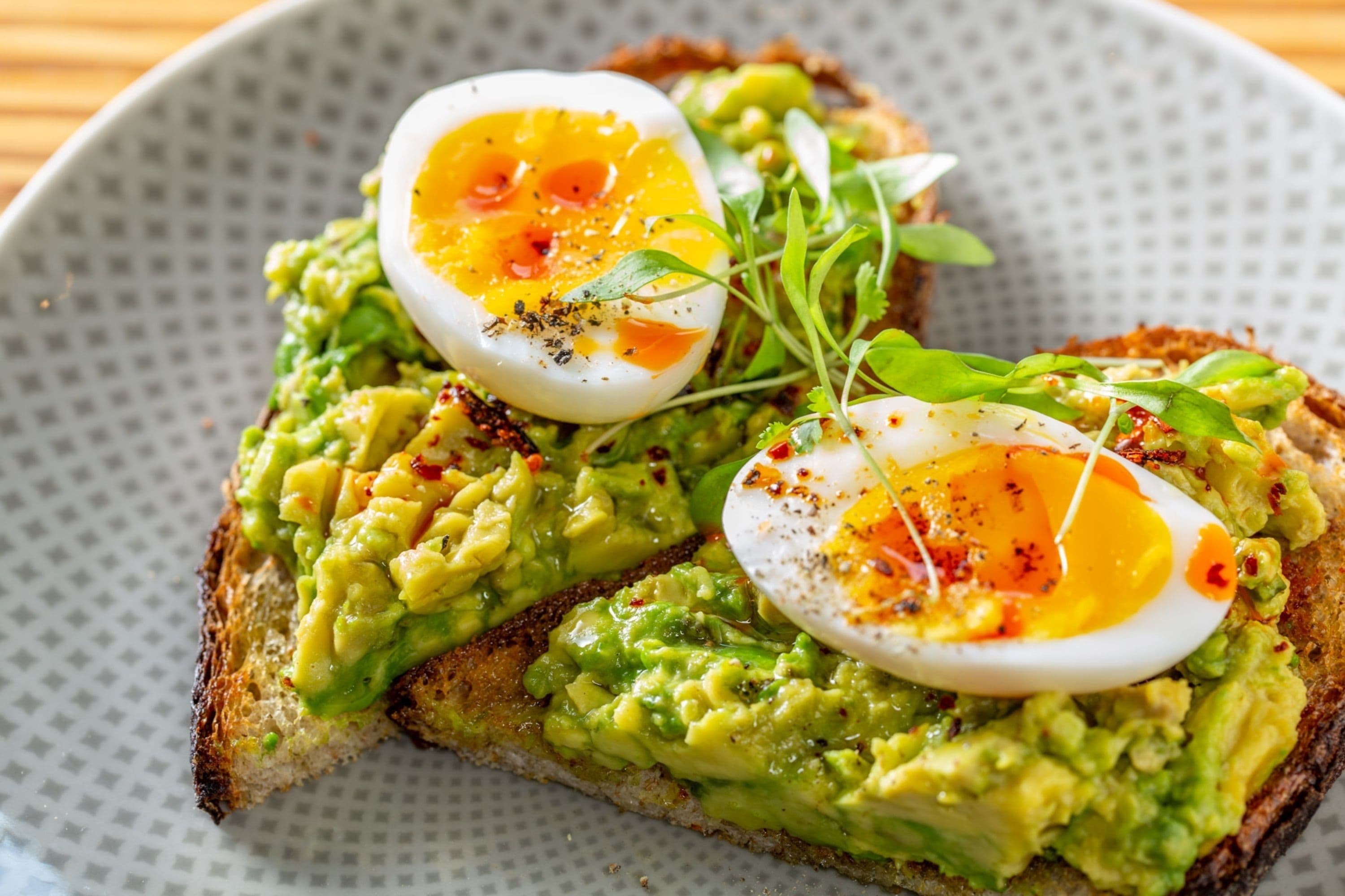 Una tostada con aguacate y un huevo duro, adornada con hierbas.