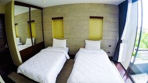 A hotel room with two beds, a large mirror, and a view of greenery through the window.
