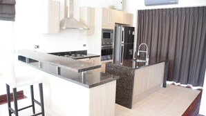 A modern kitchen with a central island, stainless steel appliances, and light wood cabinets.