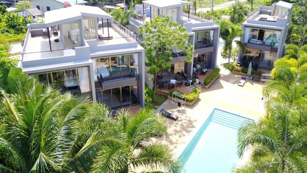 A modern resort with multiple two-story buildings, a central pool, and lush tropical surroundings.