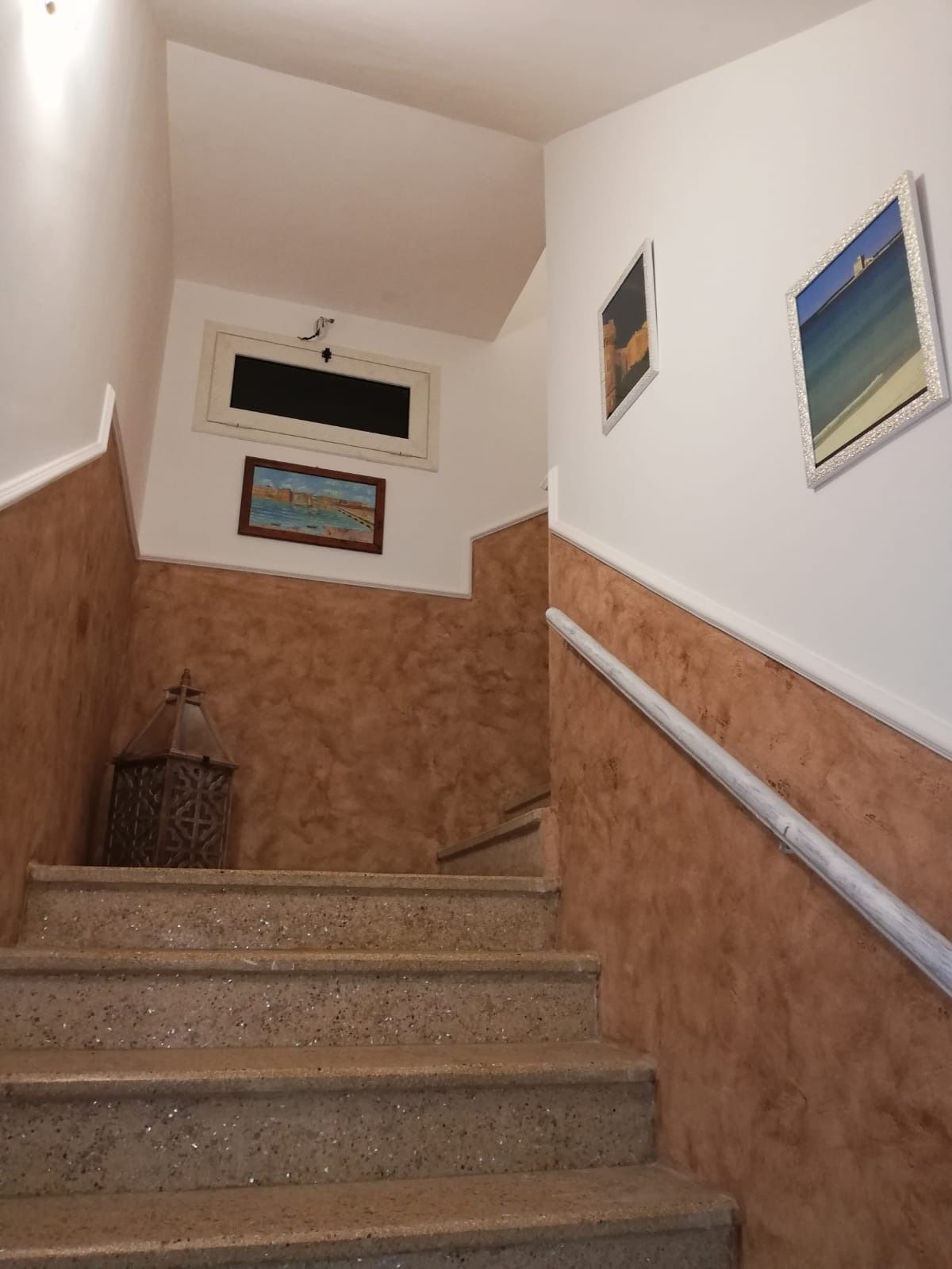 A staircase with a handrail, a small lantern, and two framed pictures on the walls.