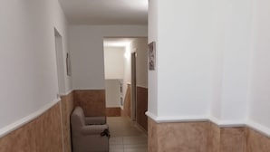 Käytävällä on beige sohva, kukkiva huonekasvi ruukussa ja käytävän päässä ovi.
