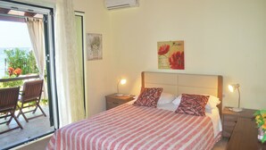 A bedroom with a bed, two bedside tables, a nightstand, a window with curtains, a chair, and a view of the outdoors. - Beachfront holiday house Eftichia (Agios Gordios)