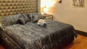 A bedroom with a tufted headboard, patterned bedspread, and a bedside lamp. - Trucountry Inn (Brady)