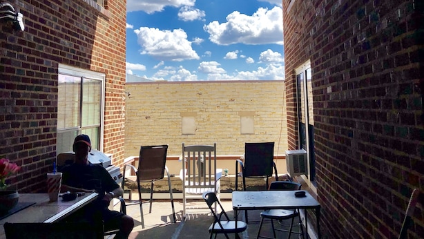 An outdoor patio with brick walls, a table, chairs, and a person sitting. - Trucountry Inn (Brady)