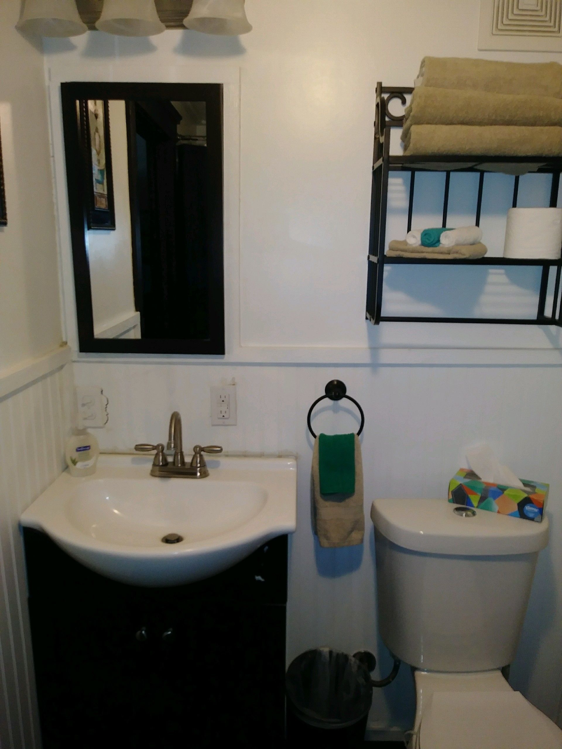 Un baño con un lavabo blanco, un espejo, un perchero con toallas, un inodoro y un cubo de basura.