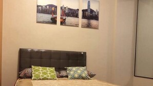 A neatly made bed with a patterned bedspread and pillows, a dark headboard, and three cityscape paintings on the wall above. - Favila Condotel Unit at 101 Newport Boulevard (Pasay)