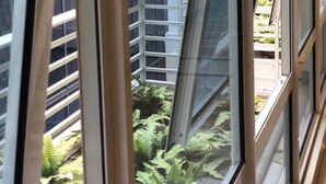 A view through a window with a metal frame, looking out at a building with multiple windows and a balcony with a railing. - Favila Condotel Unit at 101 Newport Boulevard (Pasay)