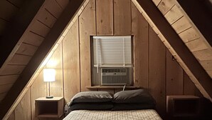 Een slaapkamer met een schuine plafond, een raam met zonwering, een bed met een geruite deken en nachtlampjes.