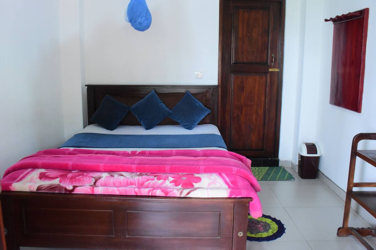 A bed with a wooden headboard, blue and pink bedding, and a blue curtain.