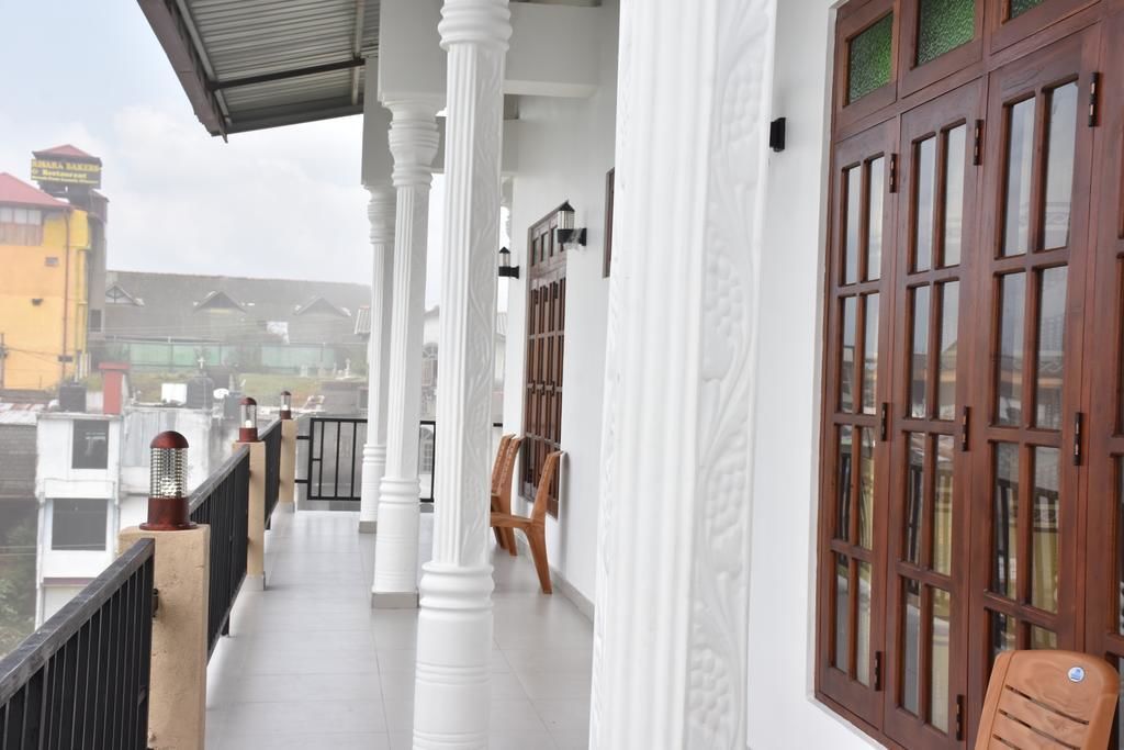 A balcony with white columns and wooden doors, overlooking a residential area.