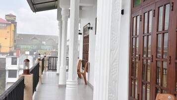 A balcony with white columns and wooden doors, overlooking a residential area.