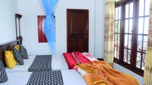 Una habitación con dos camas, una puerta de madera y un ventanal con cortinas.
