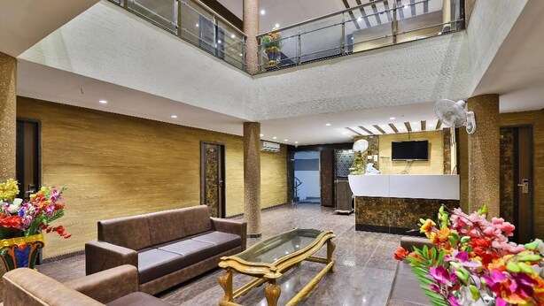 A spacious lobby with a high ceiling, a central seating area with sofas, a glass coffee table, and a reception desk. - Dev Motel & Banquet (Nadiad)