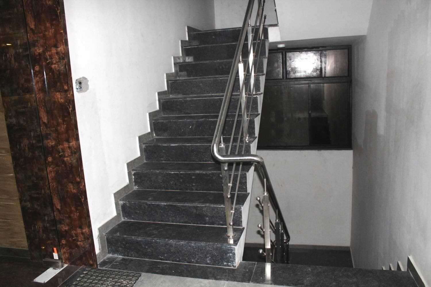 A staircase with black steps and metal handrails, leading to a landing with a dark-framed window.