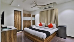 A modern hotel room with a wooden bed, a desk, a ceiling fan, and an air conditioning unit. - Dev Motel & Banquet (Nadiad)