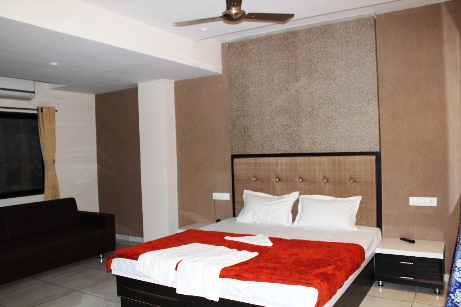 A modern bedroom with a large bed, a ceiling fan, and a dark-colored sofa.