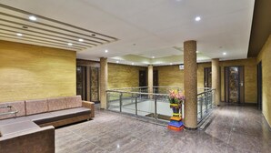 A modern lobby with a marble floor, a seating area with a sofa, a decorative vase, and a glass railing overlooking a lower level. - Dev Motel & Banquet (Nadiad)