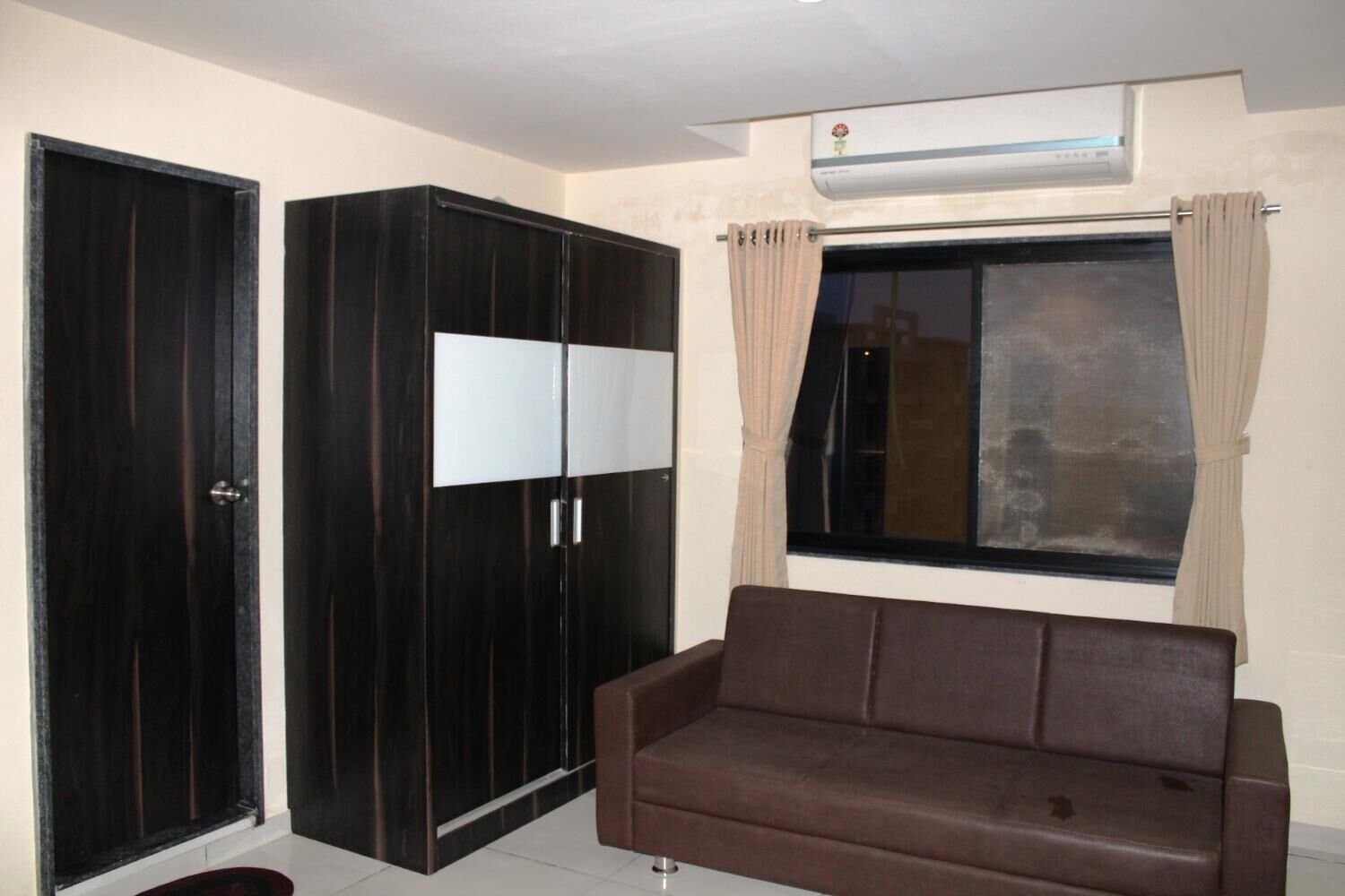 Een kamer met een bruine bank, een grote garderobe en een raam met gordijnen.
