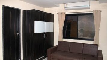 Een kamer met een bruine bank, een grote garderobe en een raam met gordijnen.