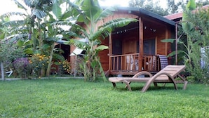 Una cabaña de madera con porche, rodeada de exuberante vegetación y césped.