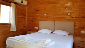 Una habitación de cabaña de madera con una cama, dos mesitas de noche y un ventanal con cortinas.