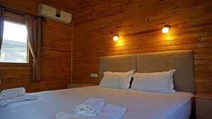 Una habitación con paneles de madera, una cama, dos almohadas y un ventanal con cortinas.