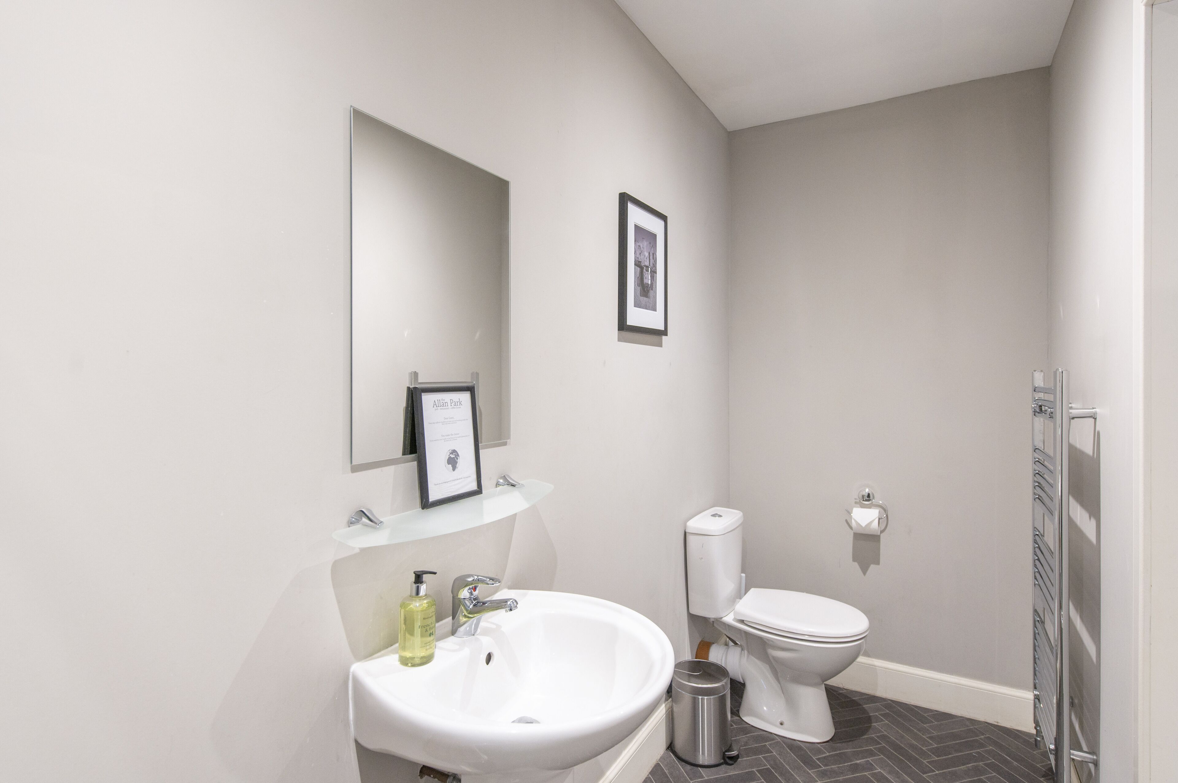 Un baño moderno con un lavamanos blanco, un certificado enmarcado, un inodoro y una zona de ducha.