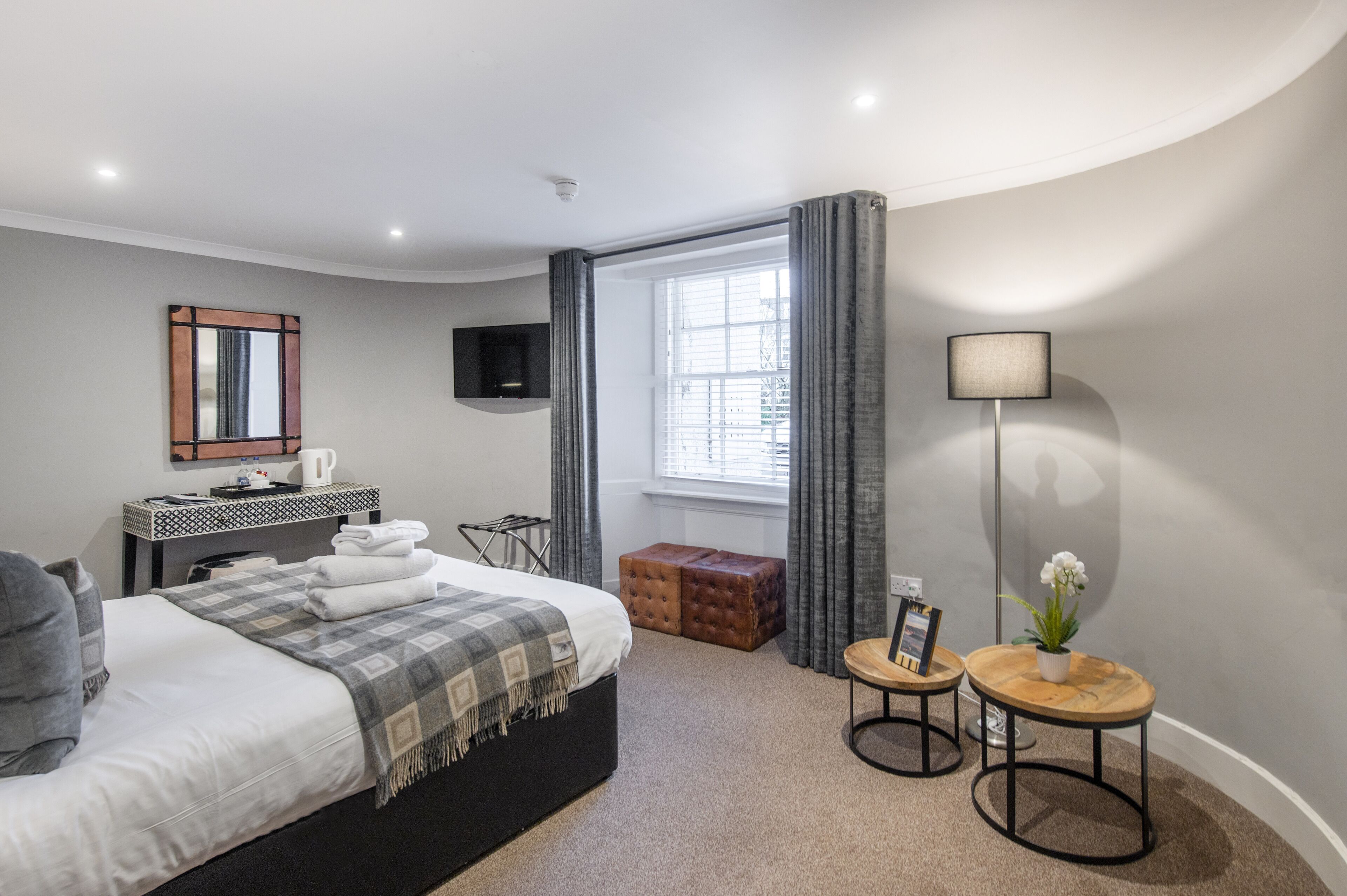 A modern hotel room with a large bed, a flat-screen TV, a bedside table with a lamp, and a window with curtains.