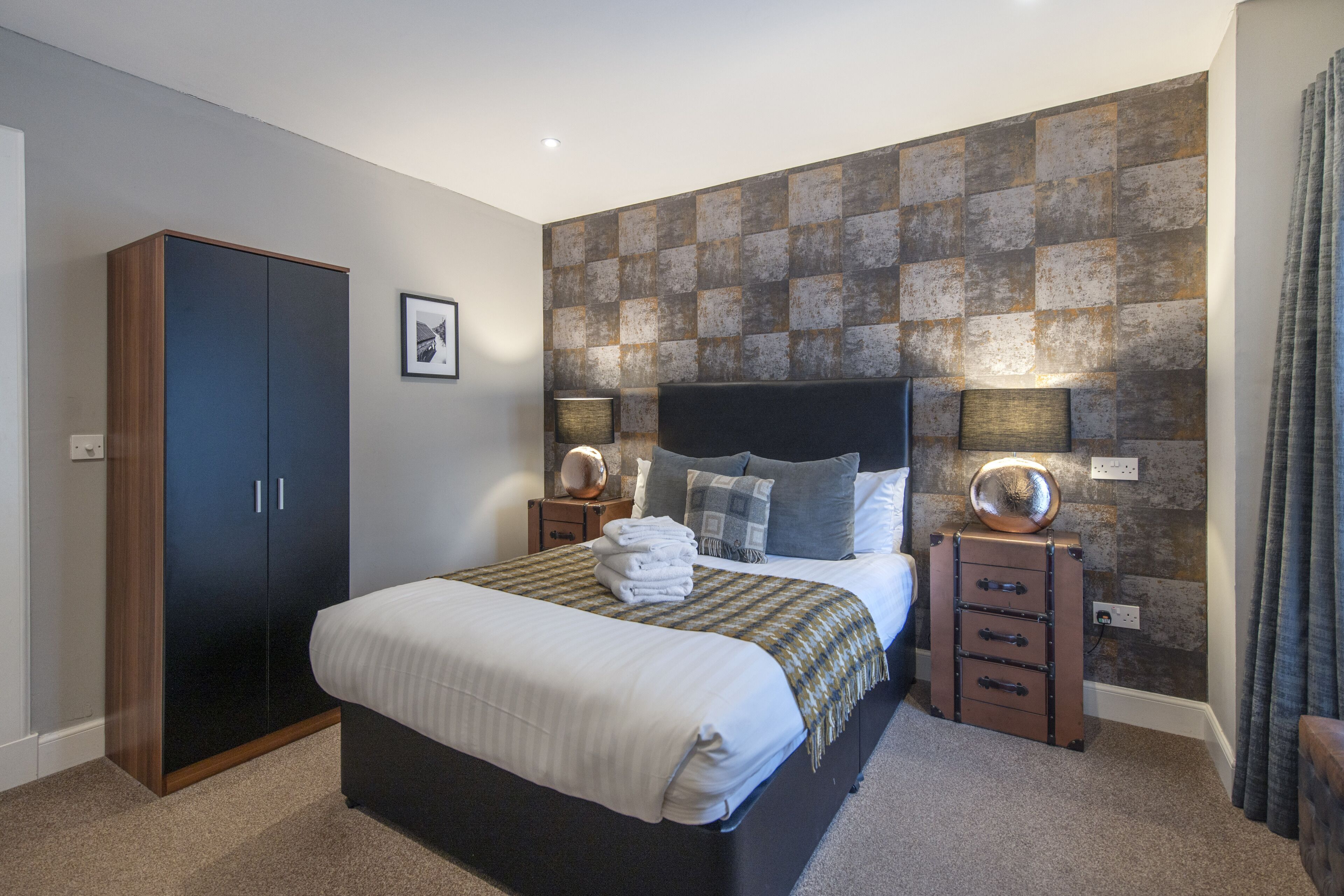 A bedroom with a bed, a wardrobe, a dresser, and a textured wall.