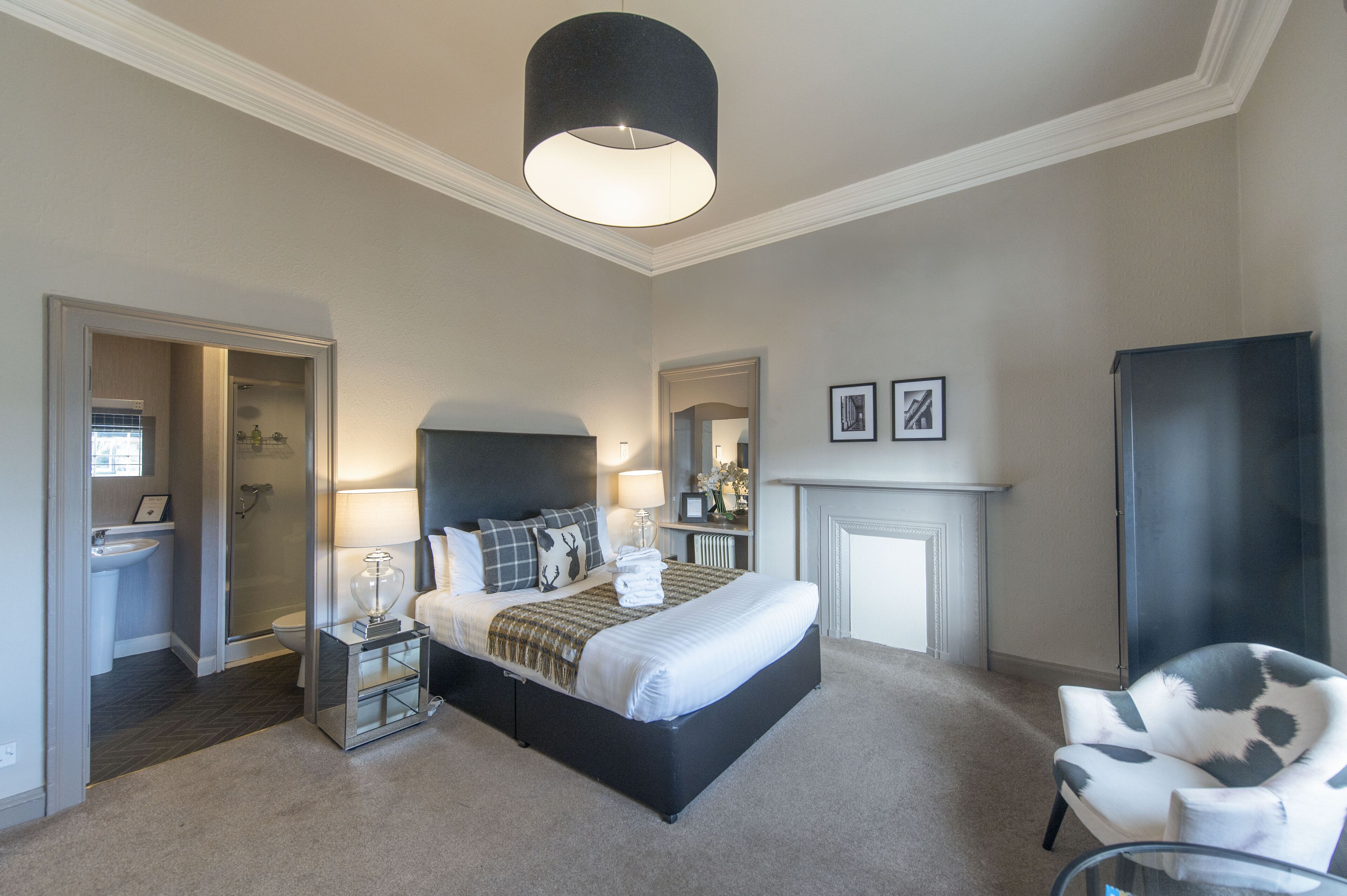 A bedroom with a large bed, bedside lamps, a chair, a fireplace, and a mirror.
