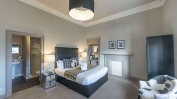 A bedroom with a large bed, bedside lamps, a chair, a fireplace, and a mirror.
