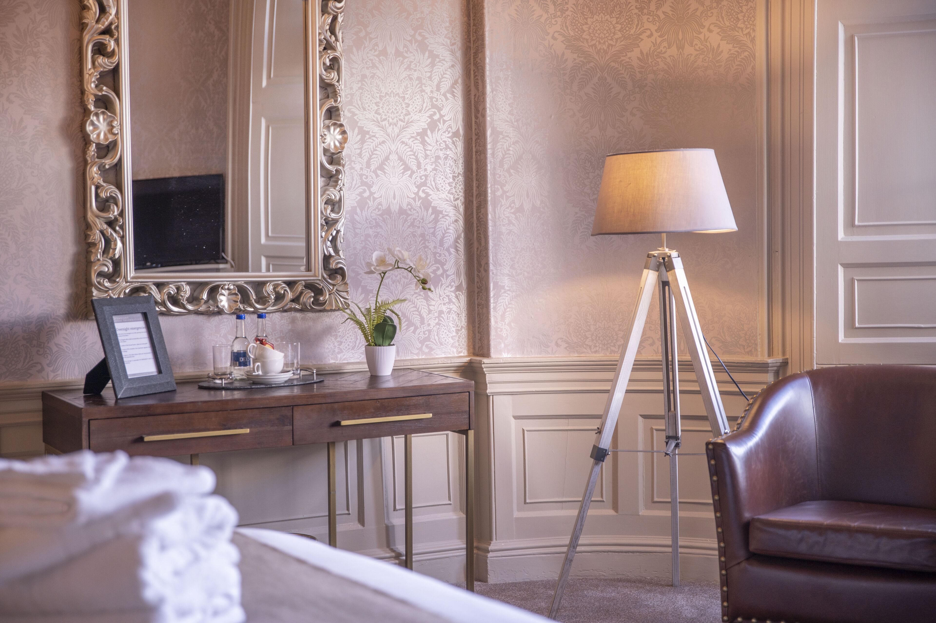Una habitación de hotel con un escritorio de madera, una lámpara, un espejo y un sillón de cuero.
