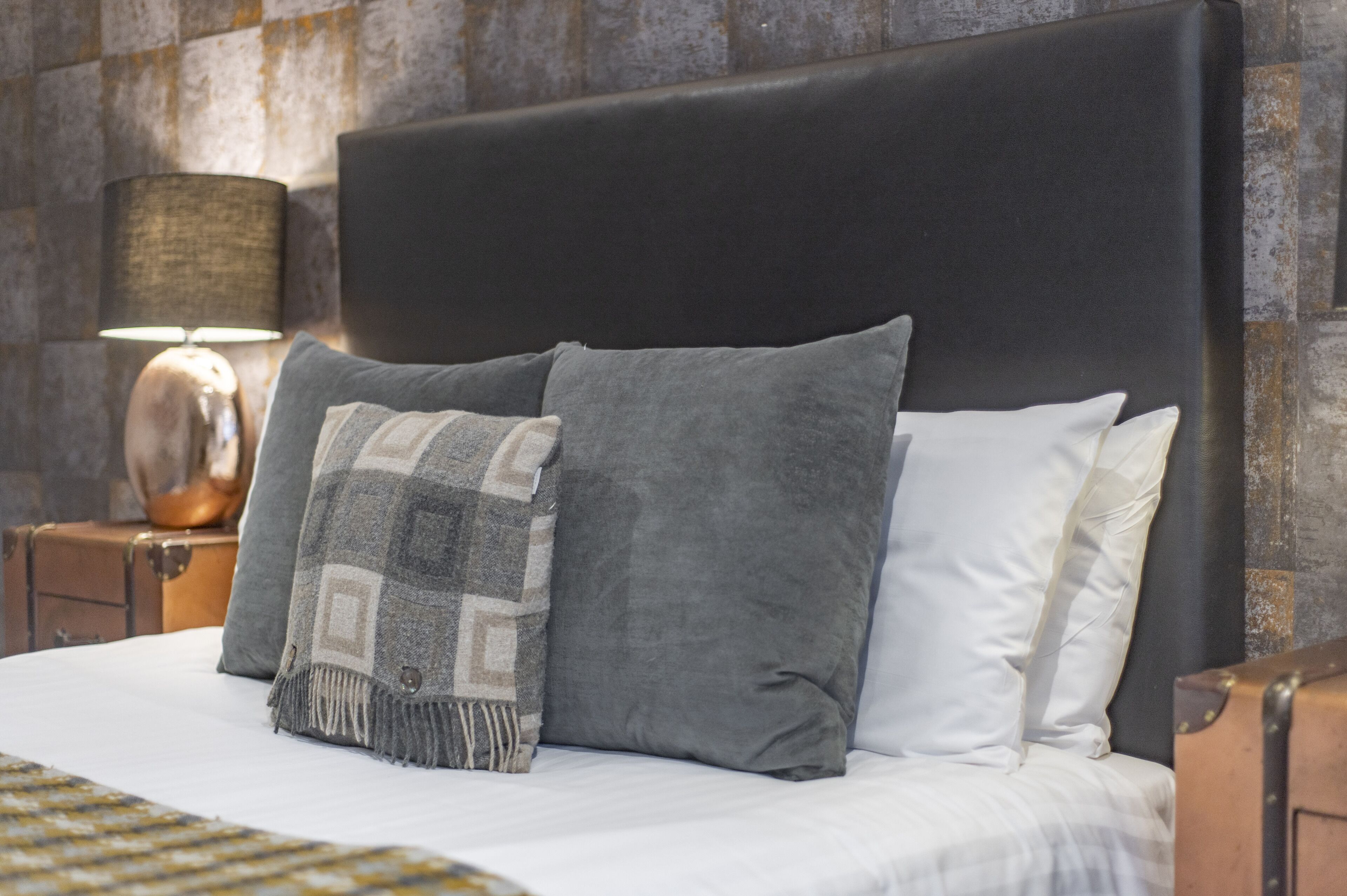 A bed with a black headboard, grey and white pillows, and a patterned throw blanket.