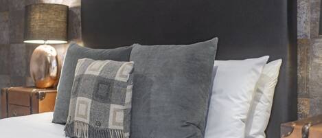 A bed with a black headboard, grey and white pillows, and a patterned throw blanket.