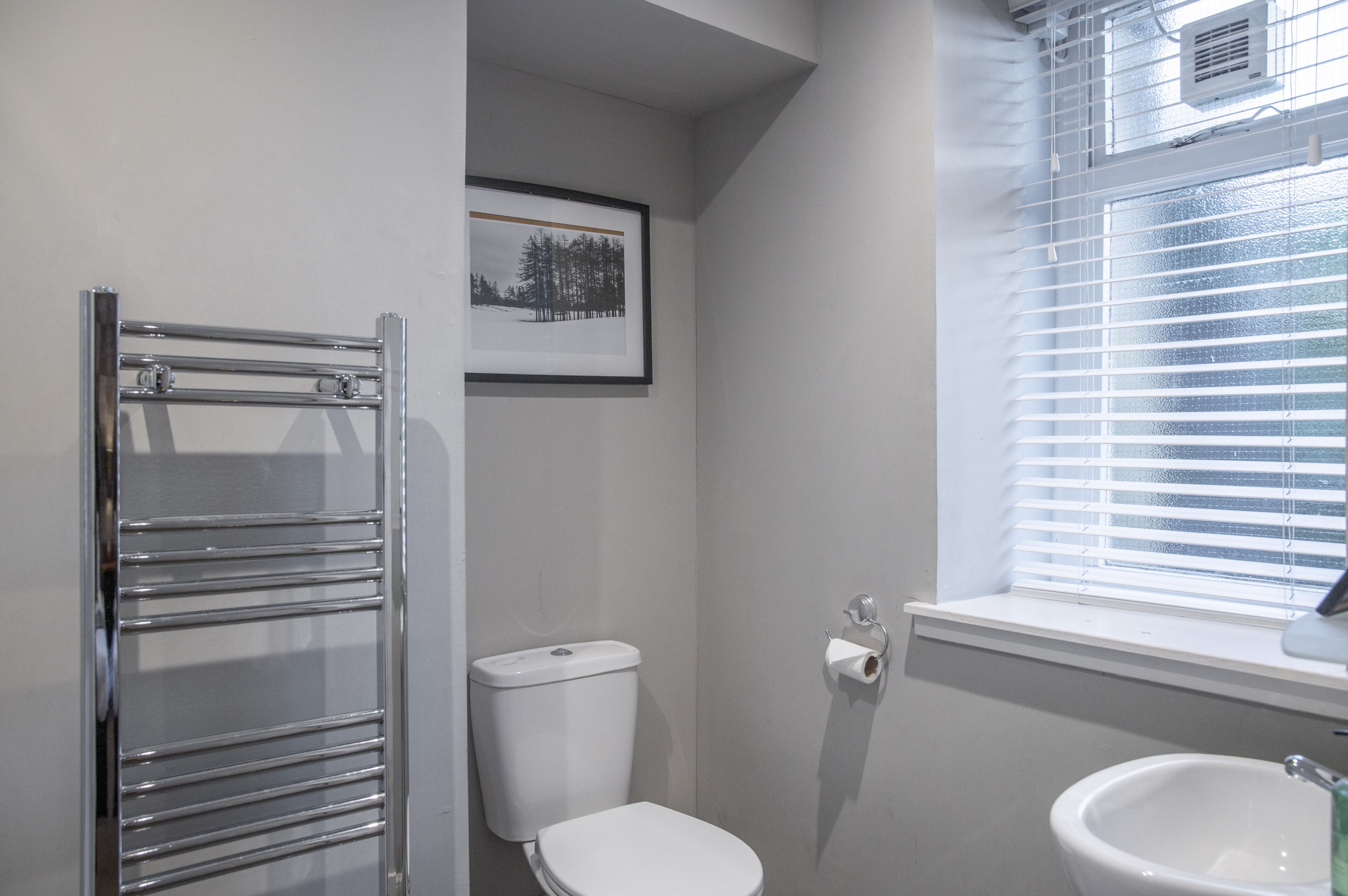 Ein Badezimmer mit Toilette, Waschbecken, Handtuchhalter und einem Fenster mit Jalousien.
