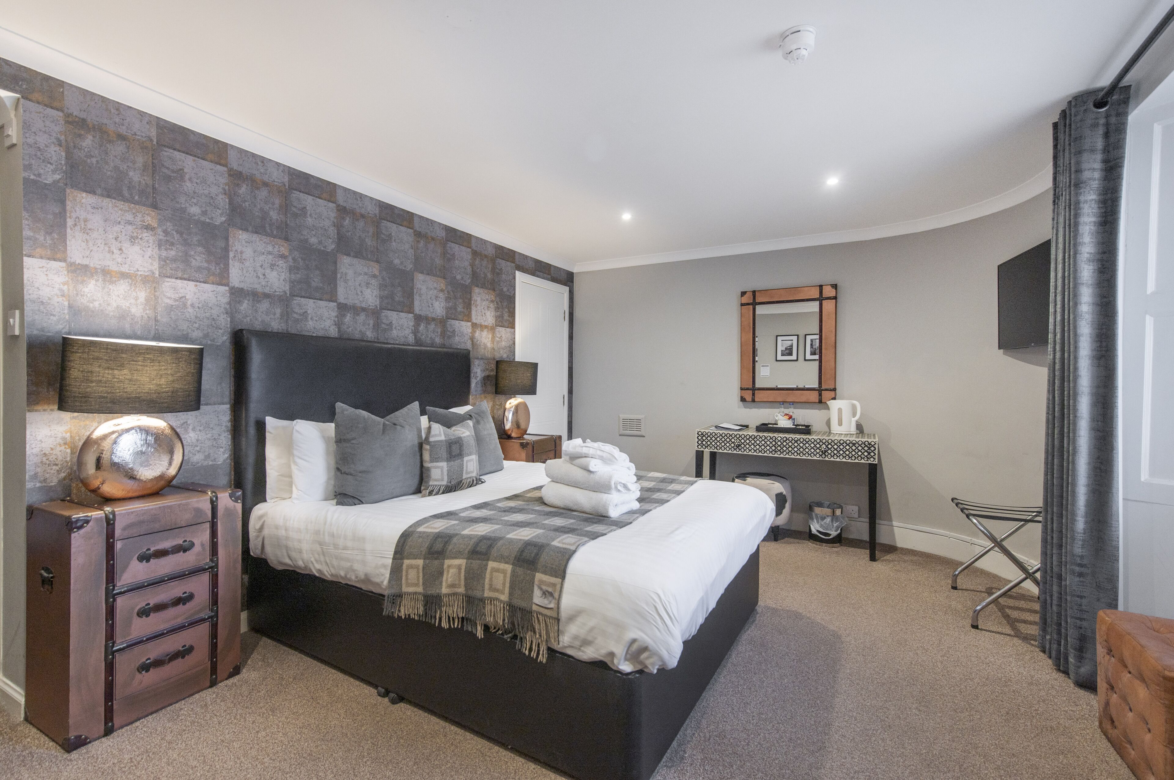 Una habitación de hotel moderna con una cama grande, un escritorio, un espejo y una maleta.