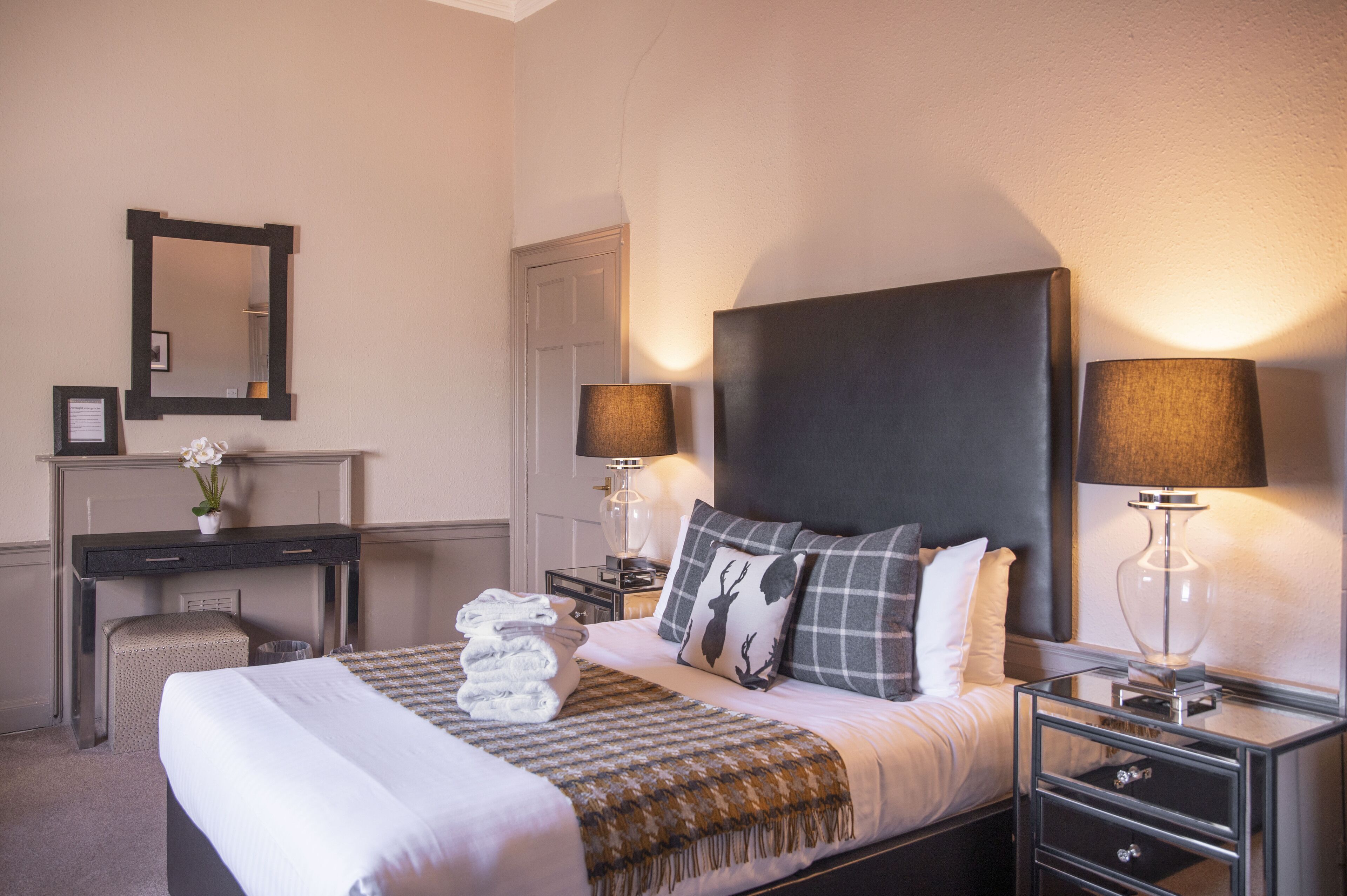 Una habitación de hotel ordenada con cama, mesitas de noche, escritorio y espejo.
