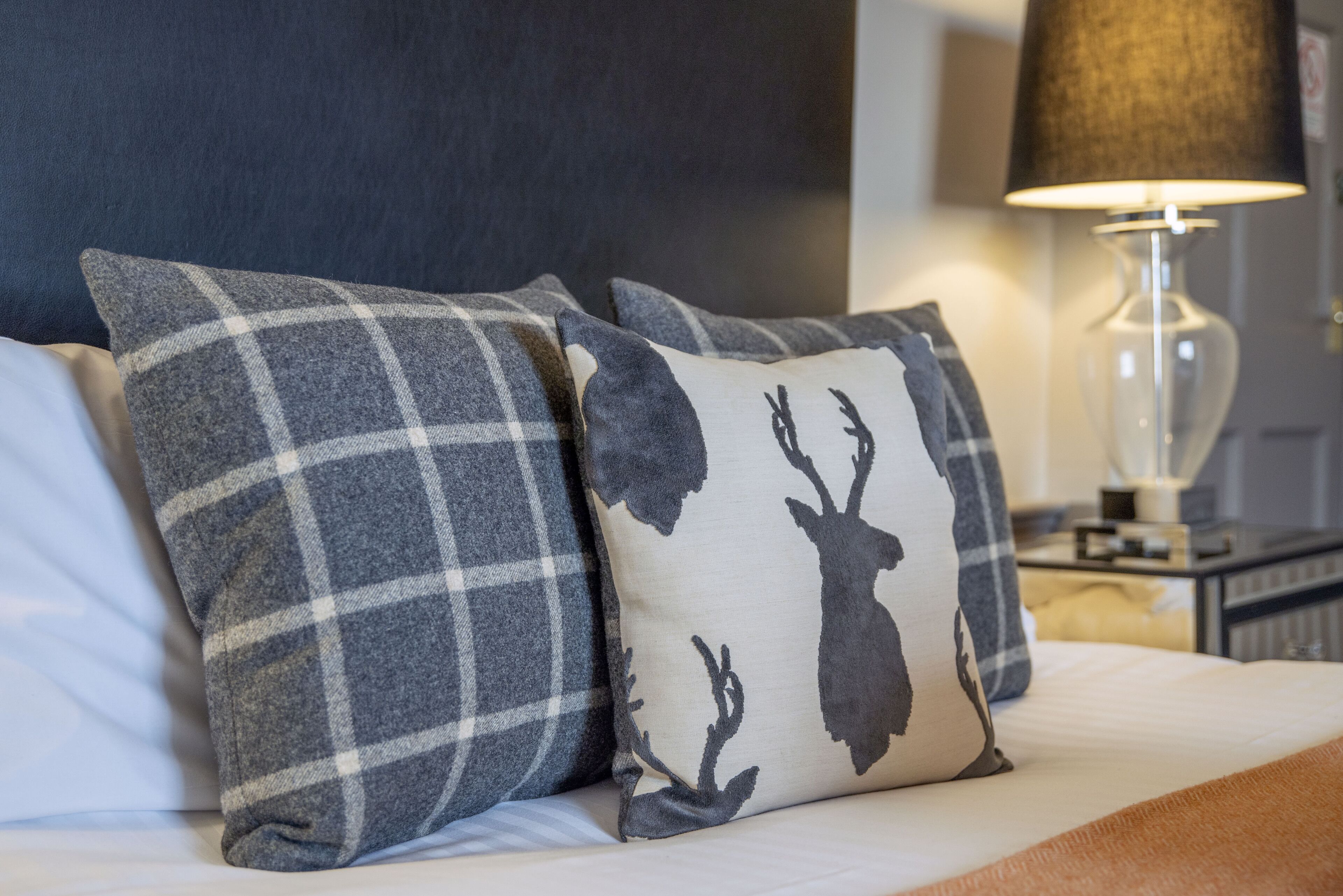 Un lit avec deux oreillers, l’un à motifs écossais et l’autre orné de la silhouette d’un cerf.