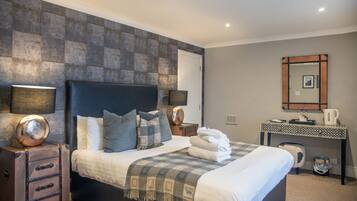 A neatly arranged bedroom with a large bed, bedside lamps, a dresser, a desk with a mirror, and a coffee maker.