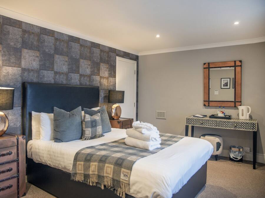 A neatly arranged bedroom with a large bed, bedside lamps, a dresser, a desk with a mirror, and a coffee maker.