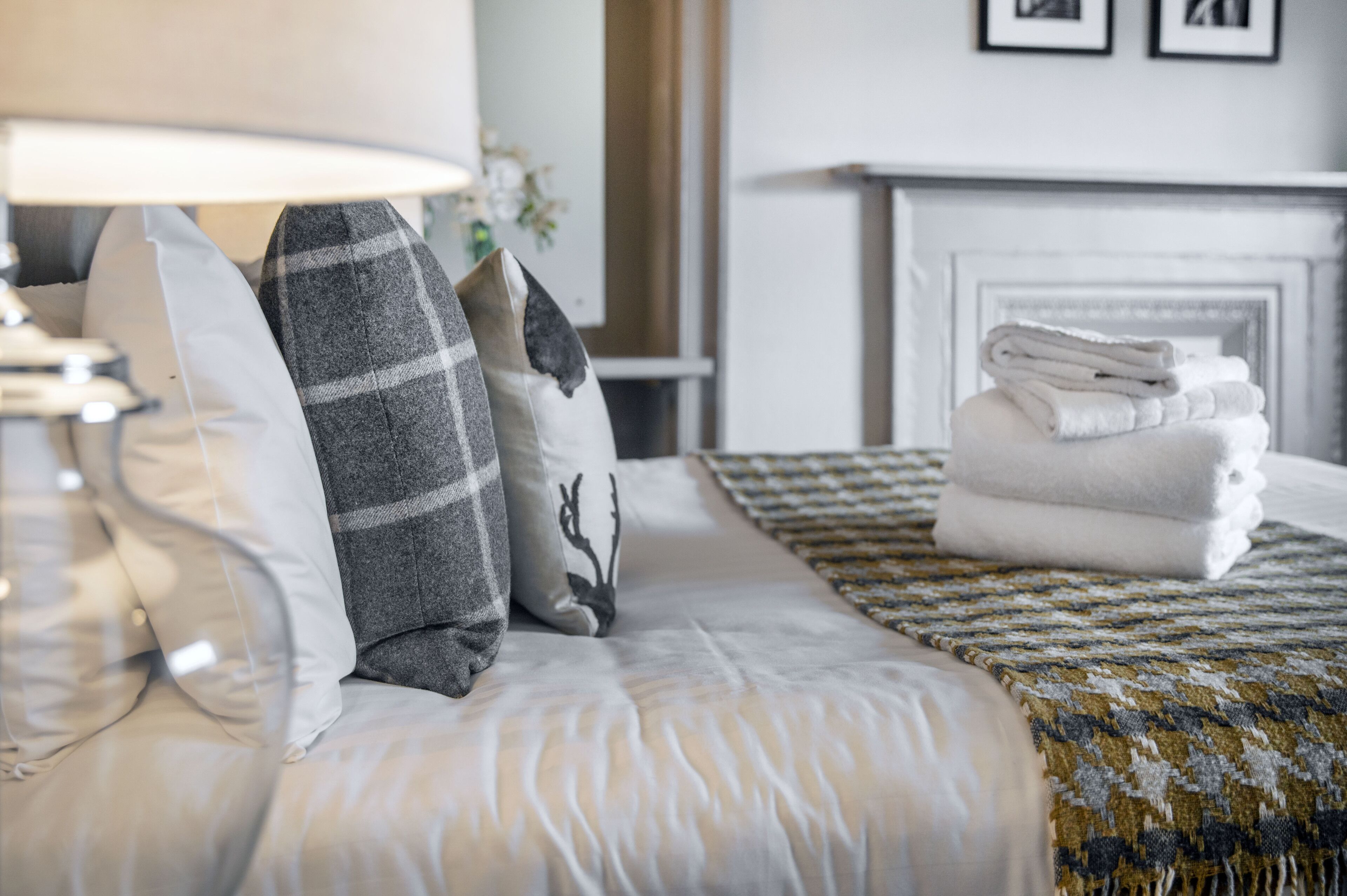 Una cama bien hecha con un edredón estampado y almohadas, una lámpara y una pila de toallas.