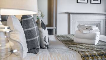 Una cama bien hecha con un edredón estampado y almohadas, una lámpara y una pila de toallas.