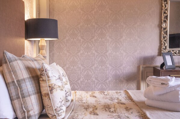 A neatly made bed with floral bedding, a lamp, and a folded towel on a nightstand.