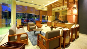 A modern hotel lobby with a reception desk, seating area, and large windows overlooking a parking area. - Wood Note Thekkady (Peermade)