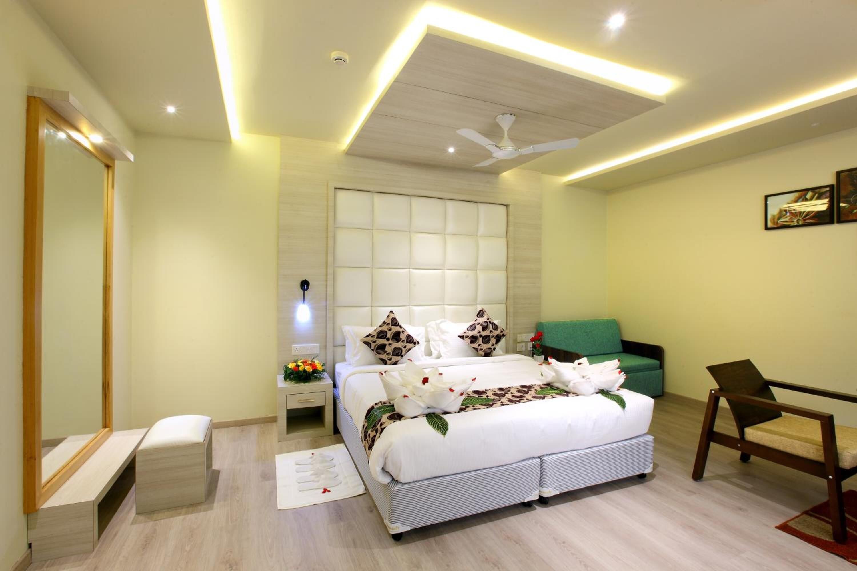 A modern bedroom with a large bed, a ceiling fan, a green armchair, and a bedside table with a lamp.