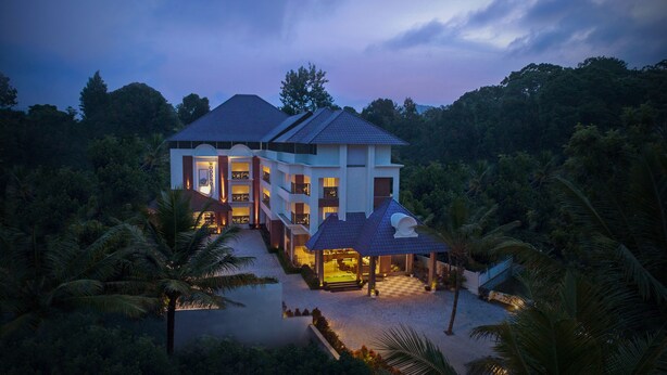 A large, multi-story hotel with a prominent entrance and a covered outdoor area. - Wood Note Thekkady (Peermade)