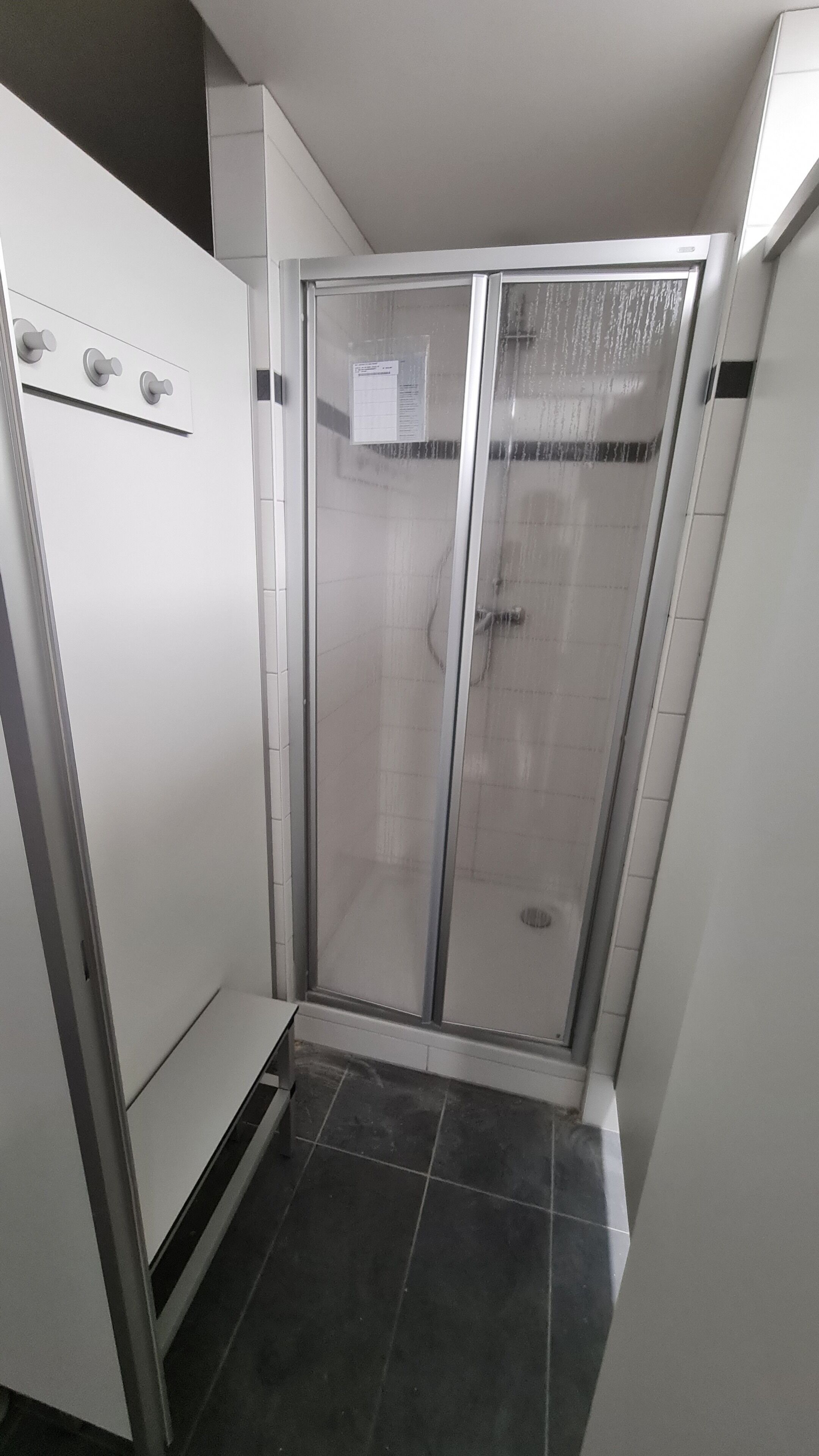 Eine Dusche mit Glastür, einer weißen Wand und einem gefliesten Boden.
