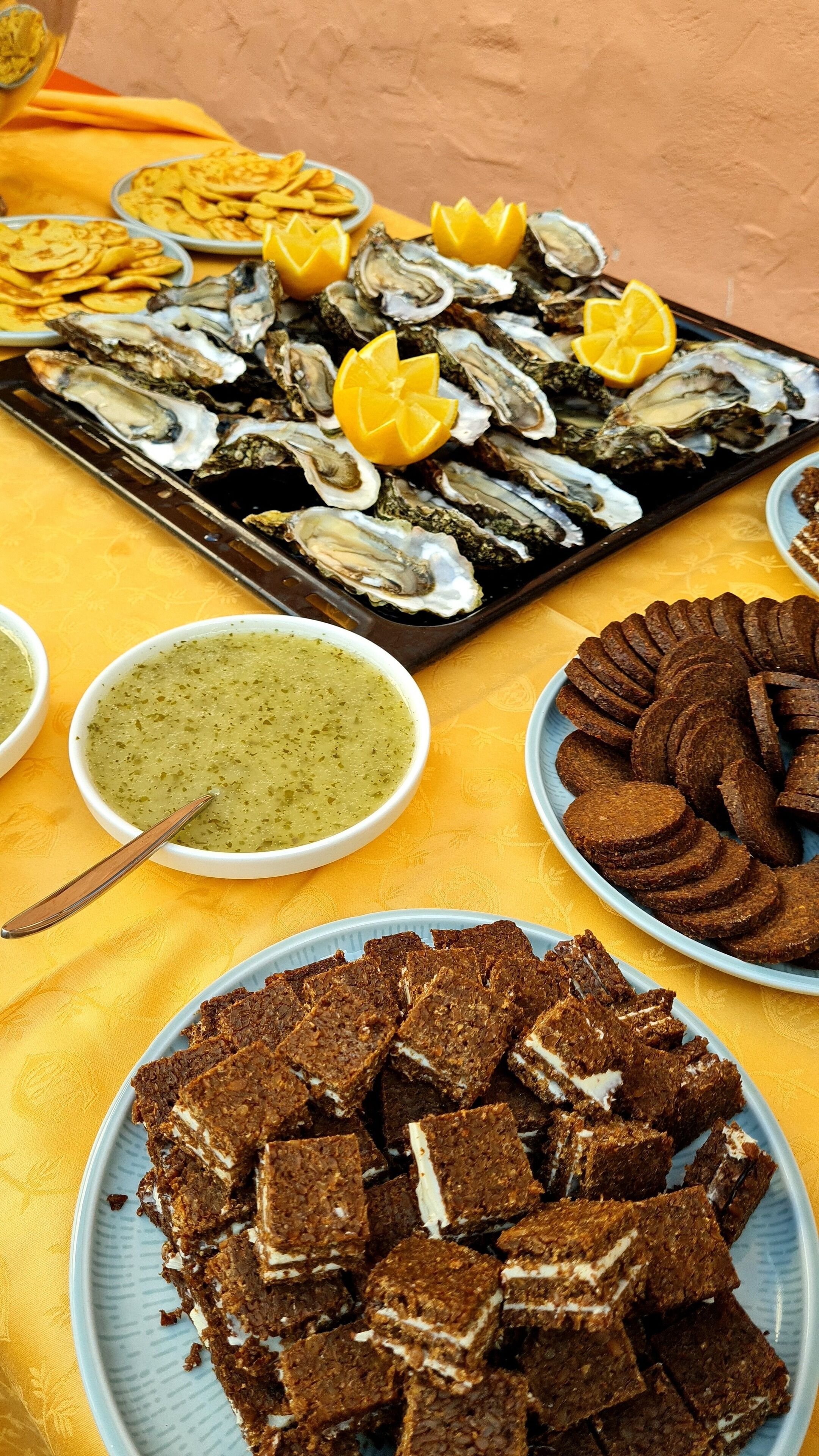 A tray of oysters garnished with lemon slices, a bowl of green soup, and a plate of brownies.